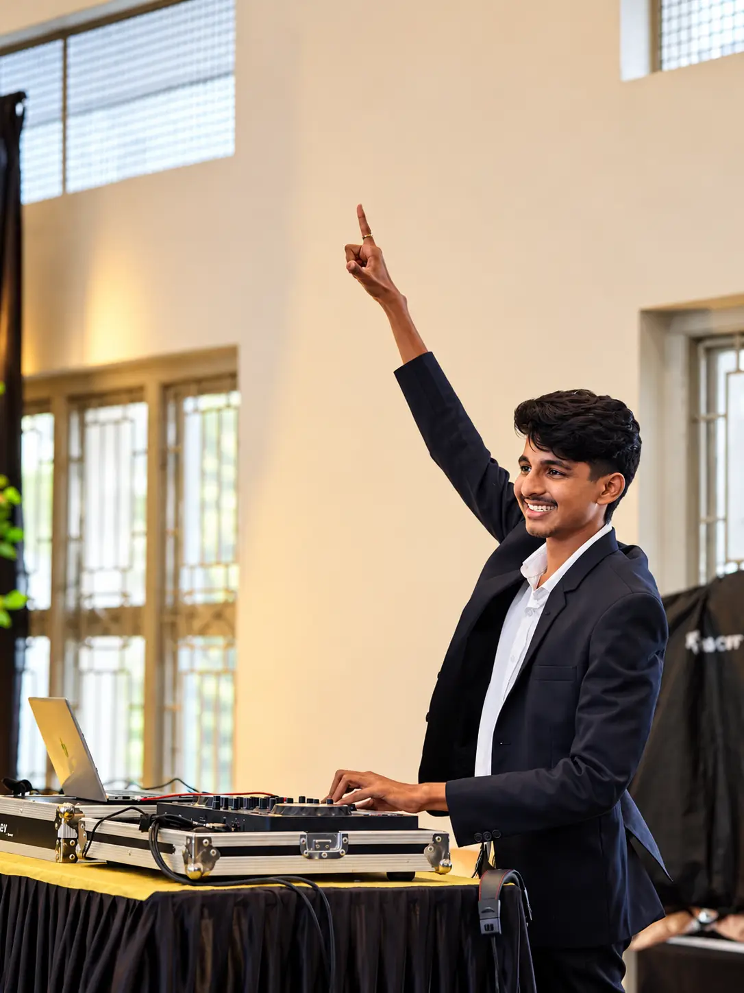 DJ Rev in a blazer raising a hand to the crowd from the decks