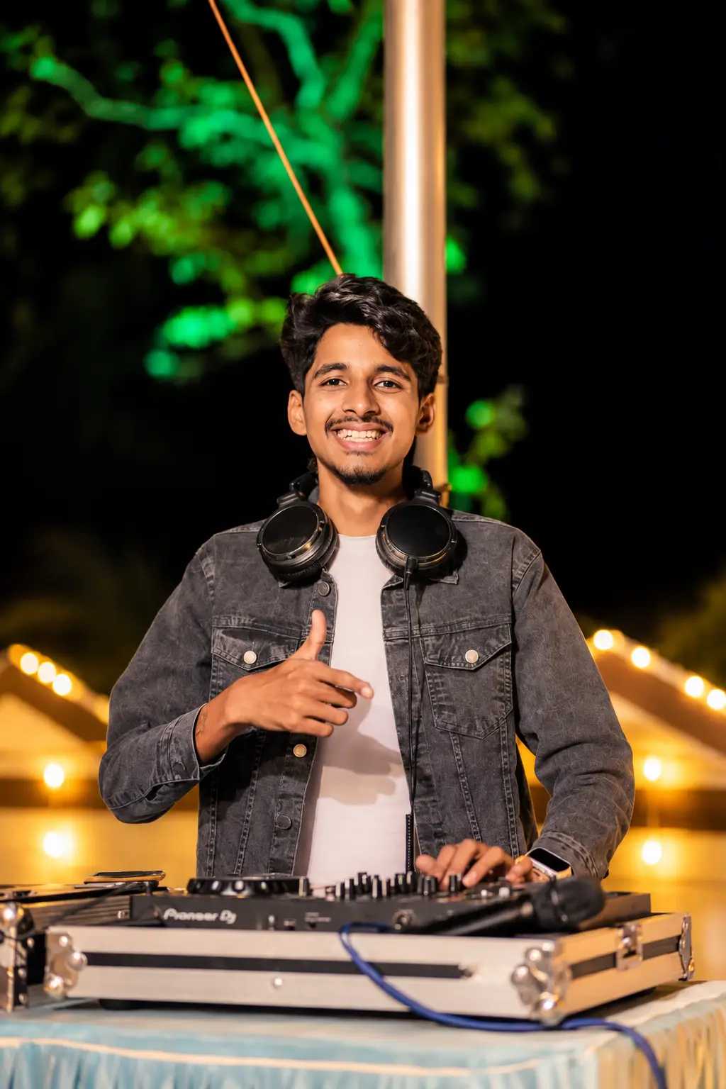 DJ Rev in a denim jacket giving a thumbs up at an outdoor night function