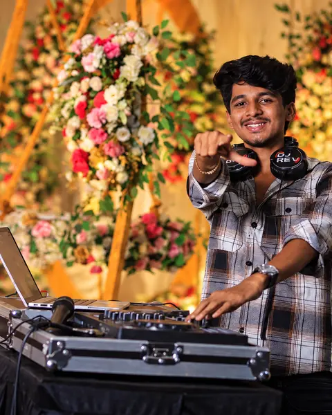 DJ Rev pointing at the camera from his console beside a floral wedding stage