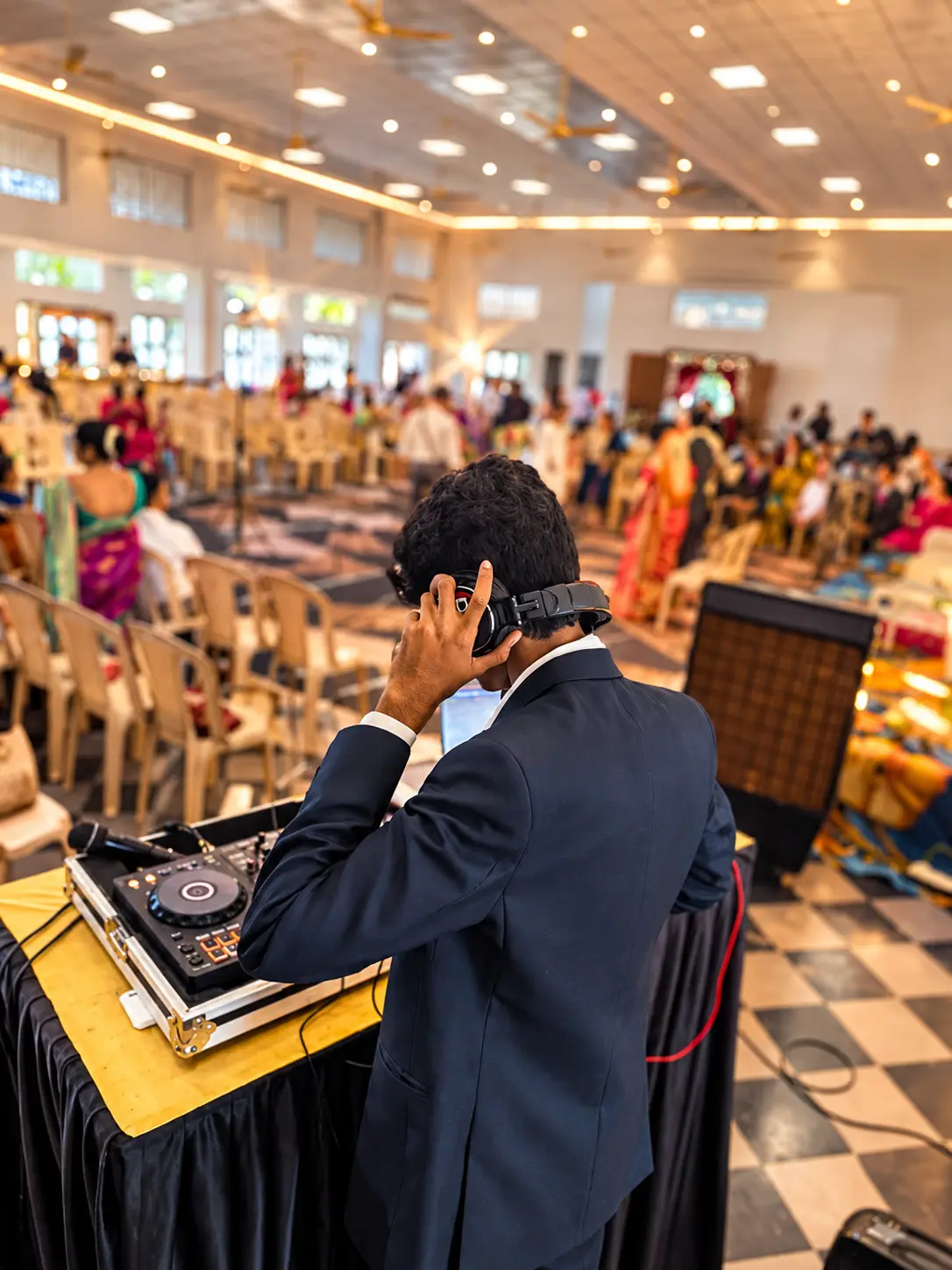 DJ Rev on headphones cueing a track as reception guests fill the hall