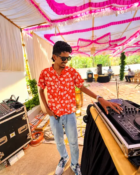 DJ Rev at his console under a decorated pandal with sound gear behind