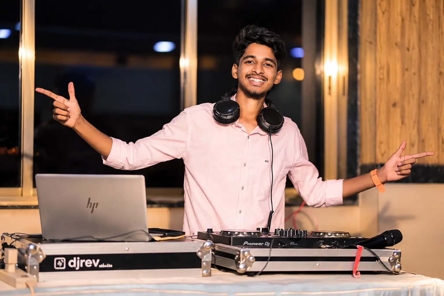 DJ Rev with arms outstretched behind his console at an evening event