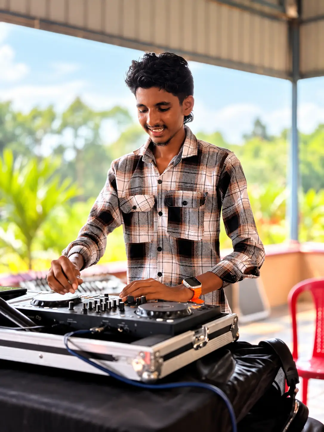 DJ Rev mixing on a rooftop terrace in daylight with palm trees behind